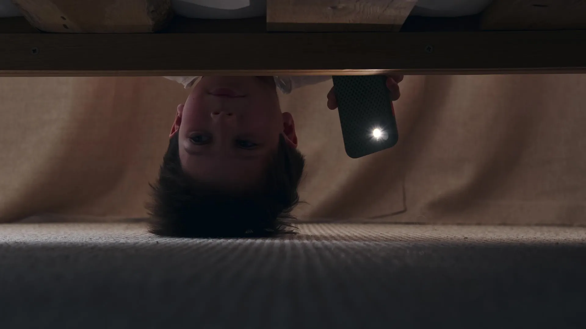 kid using phone as a flashlight to look for something under a bed